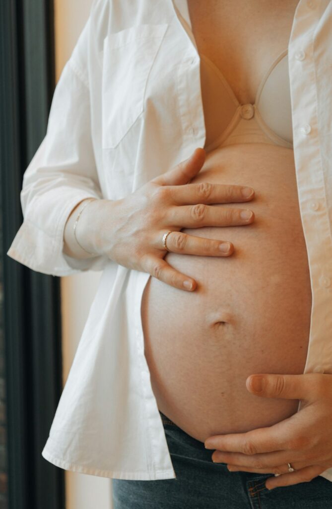 A pregnant woman gently brushing her teeth in a bright bathroom with a soft toothbrush.