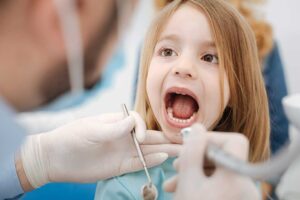 Child receiving a dental sealant while a clinician protects and examines a back molar.